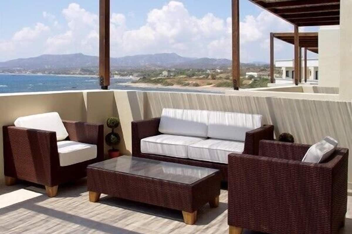 Una terraza con mobiliario de mimbre, un sofá blanco y una mesita de centro.