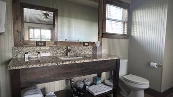 A bathroom with a wooden vanity, a sink, a mirror, a toilet, and a window with blinds.