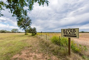 A sign for a River Trail with a dirt path leading into a grassy field. - Vineyard Trail Cottages - Adults Only (Fredericksburg)