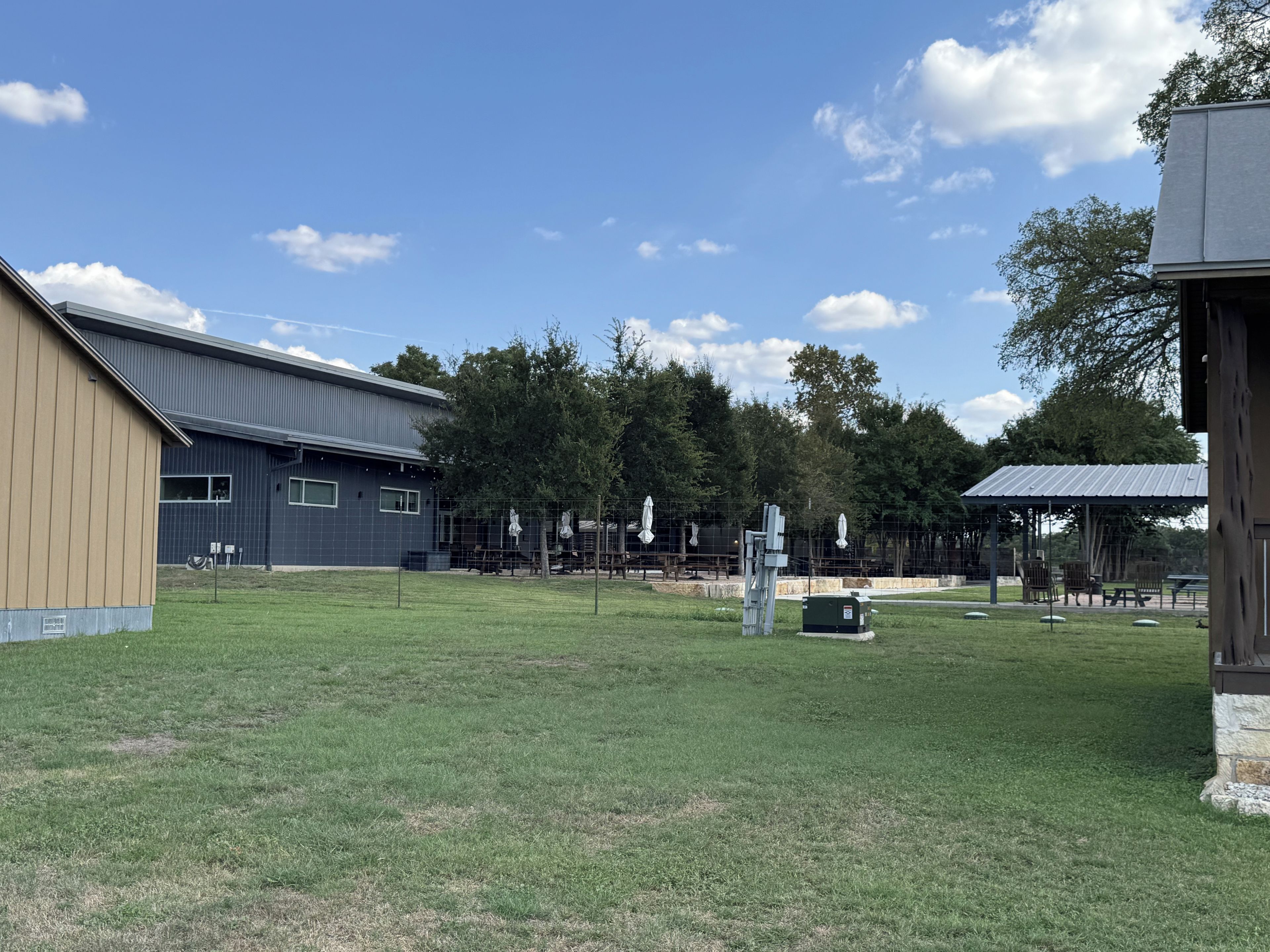 A grassy area with a building, a fenced playground, and a covered seating area.