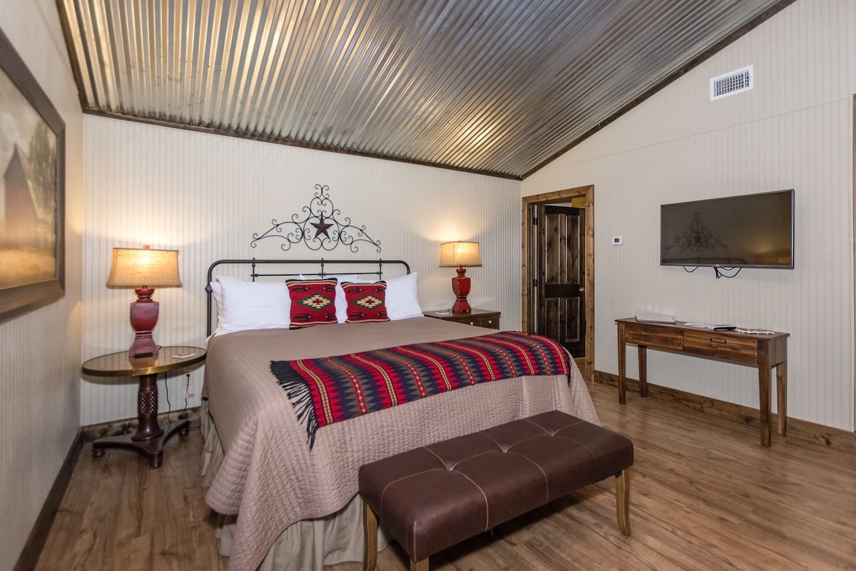 A bedroom with a bed, bedside lamps, a television, a wooden bench, and a door.