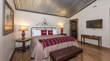 A bedroom with a bed, bedside lamps, a television, a wooden bench, and a door.