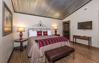 Een slaapkamer met een bed, nachtlampjes, een televisie, een houten bankje en een deur.