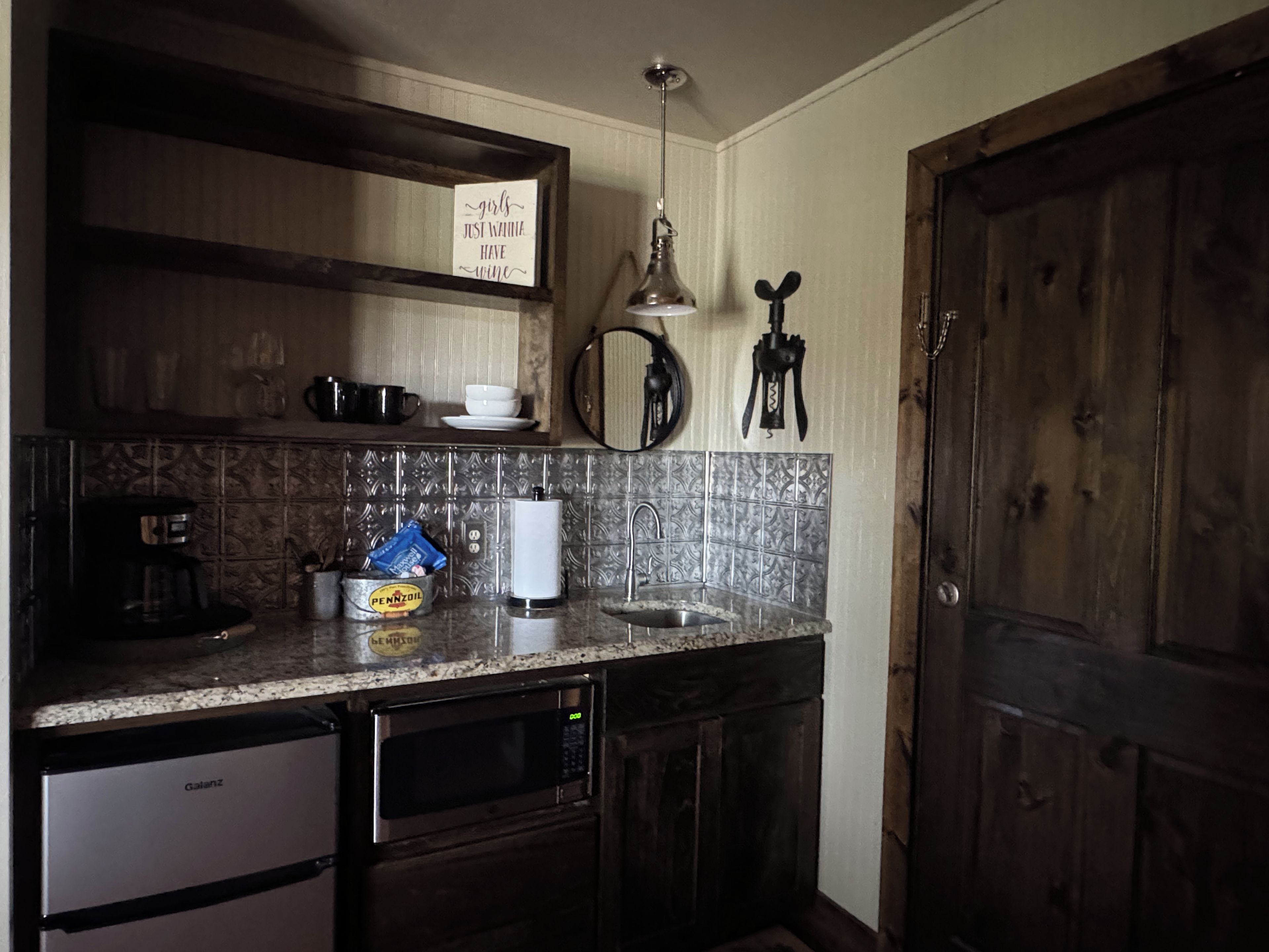 A kitchen with a coffee maker, a kettle, a dish rack, and a sign on the wall.