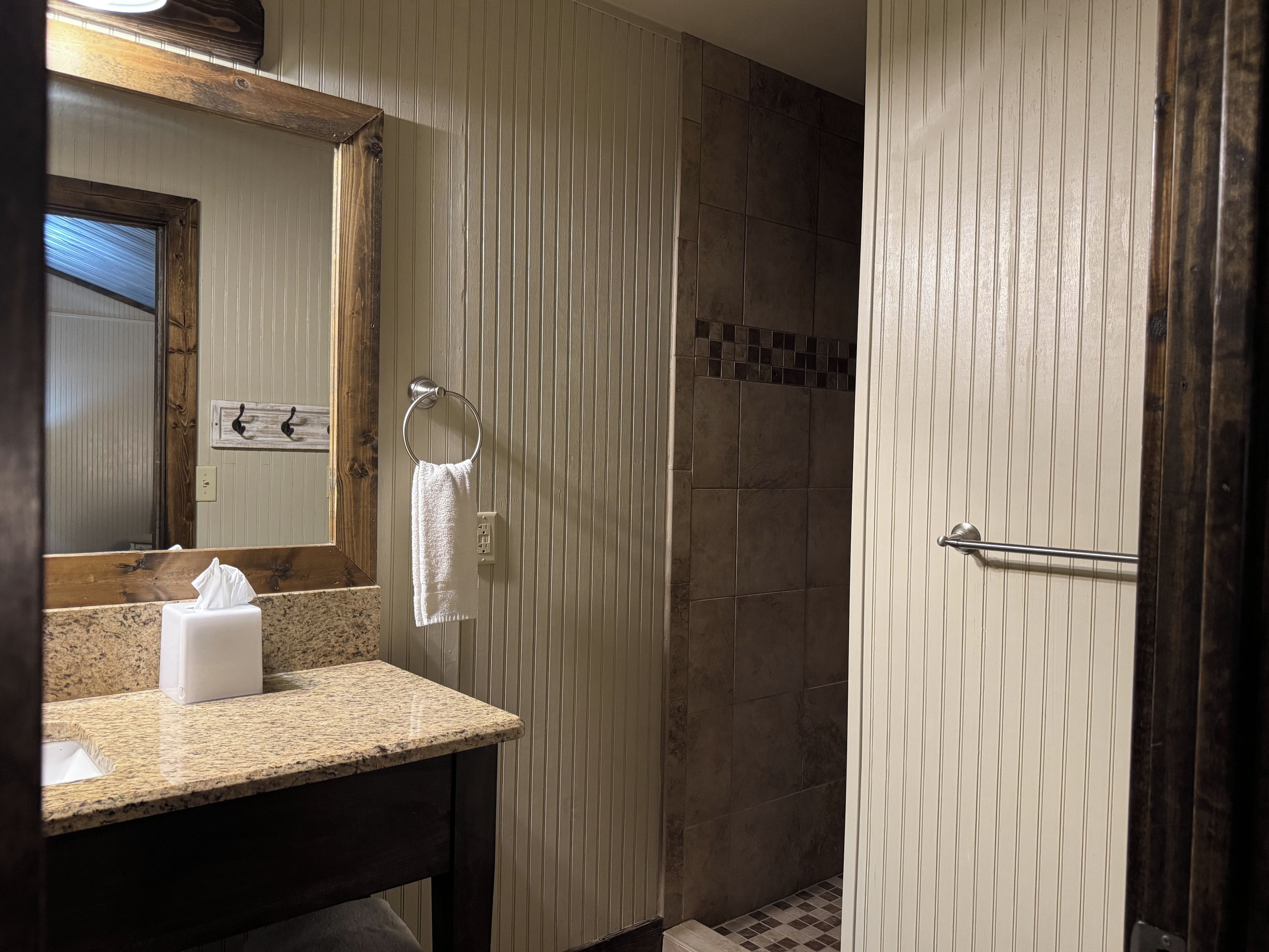 A bathroom with a granite countertop, a mirror, a towel rack, and a shower area.