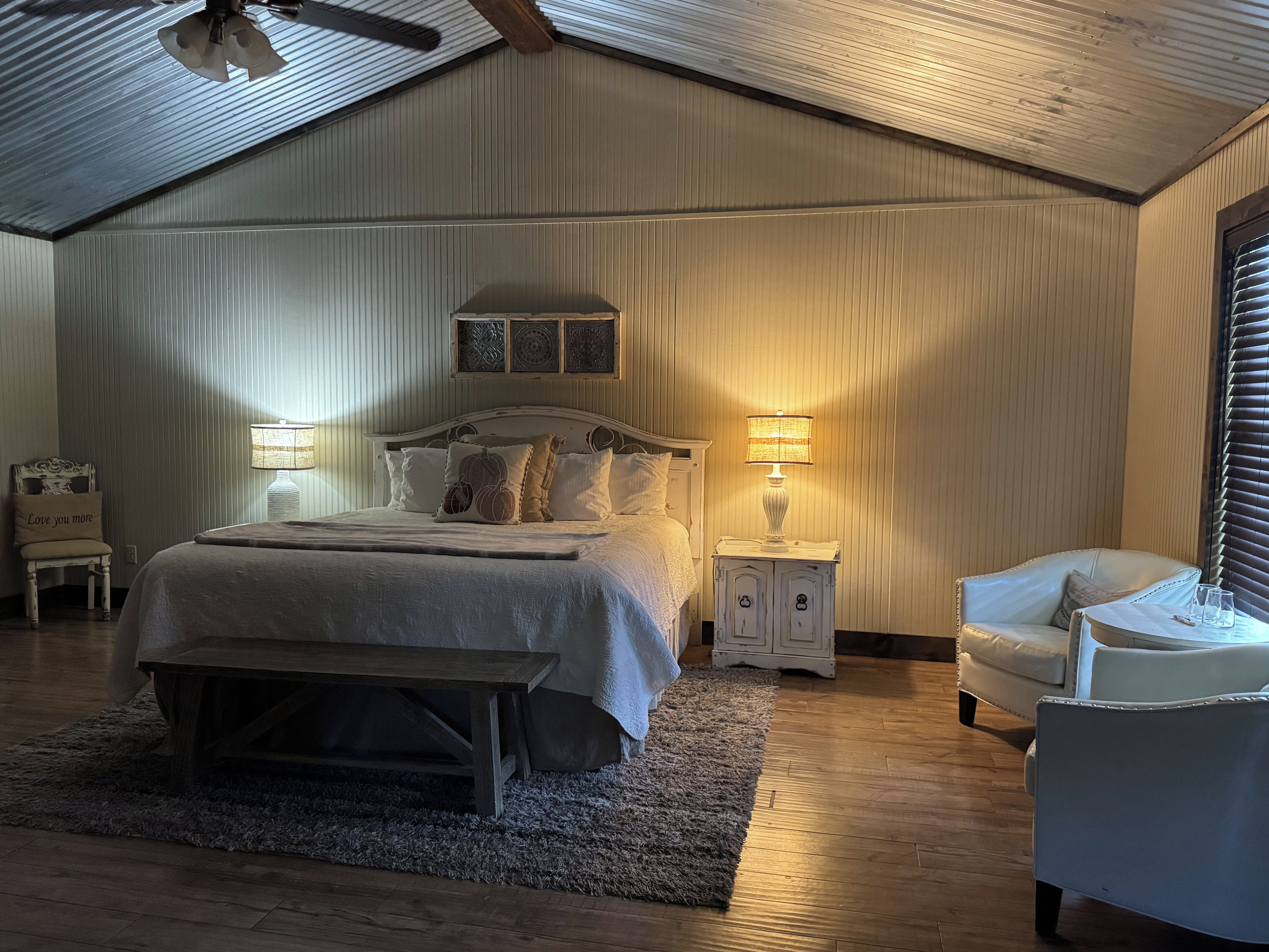 Ein Schlafzimmer mit einem großen Bett, Nachttischlampen, einem Sessel und einer Holzbank.