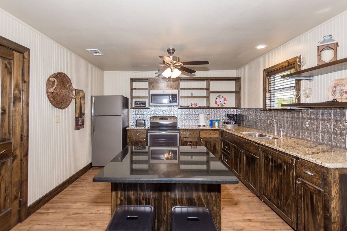 Una cocina moderna con una isla central, armarios de madera, microondas y ventilador de techo.