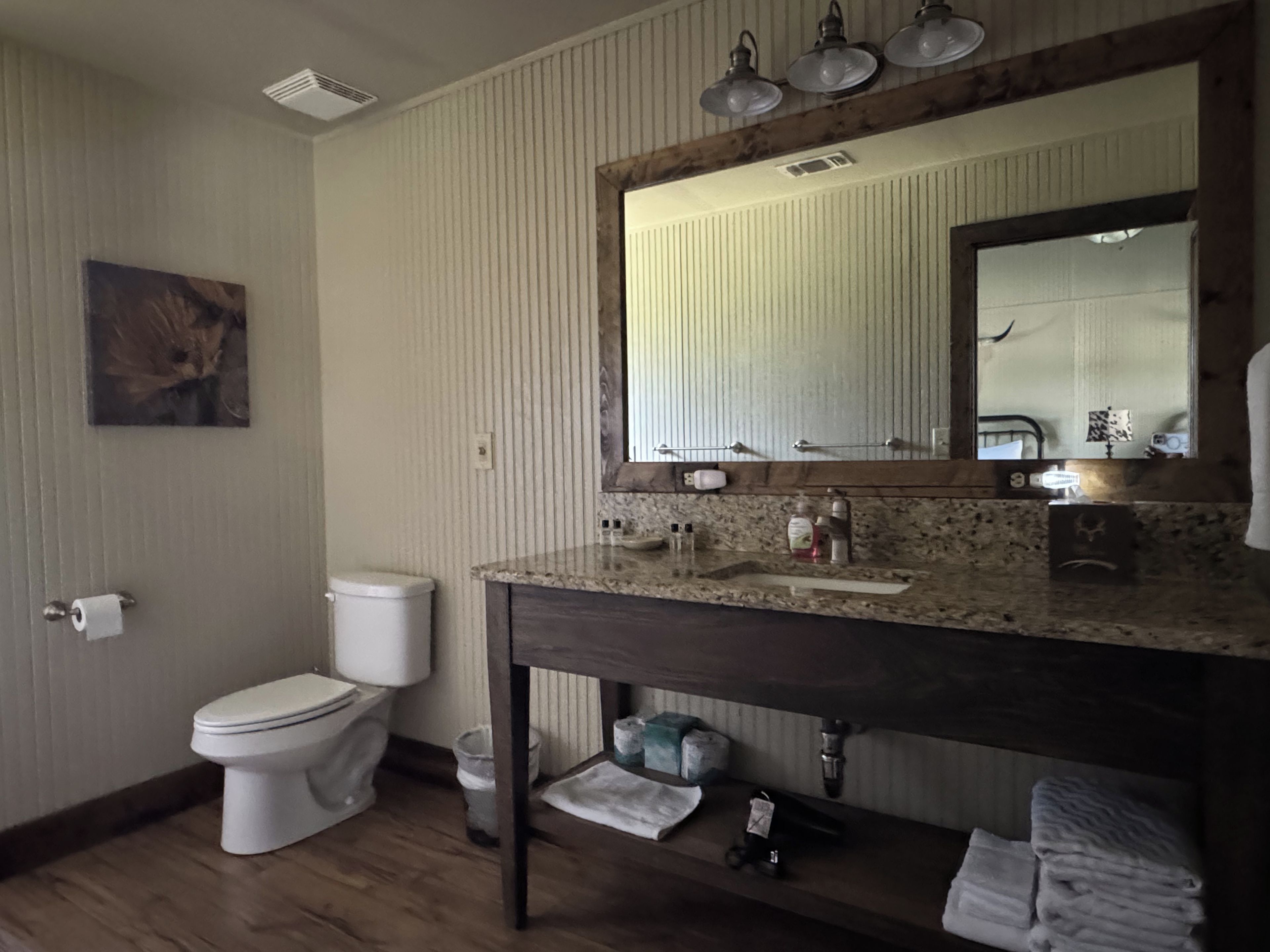 A bathroom with a toilet, sink, mirror, and wooden floor.