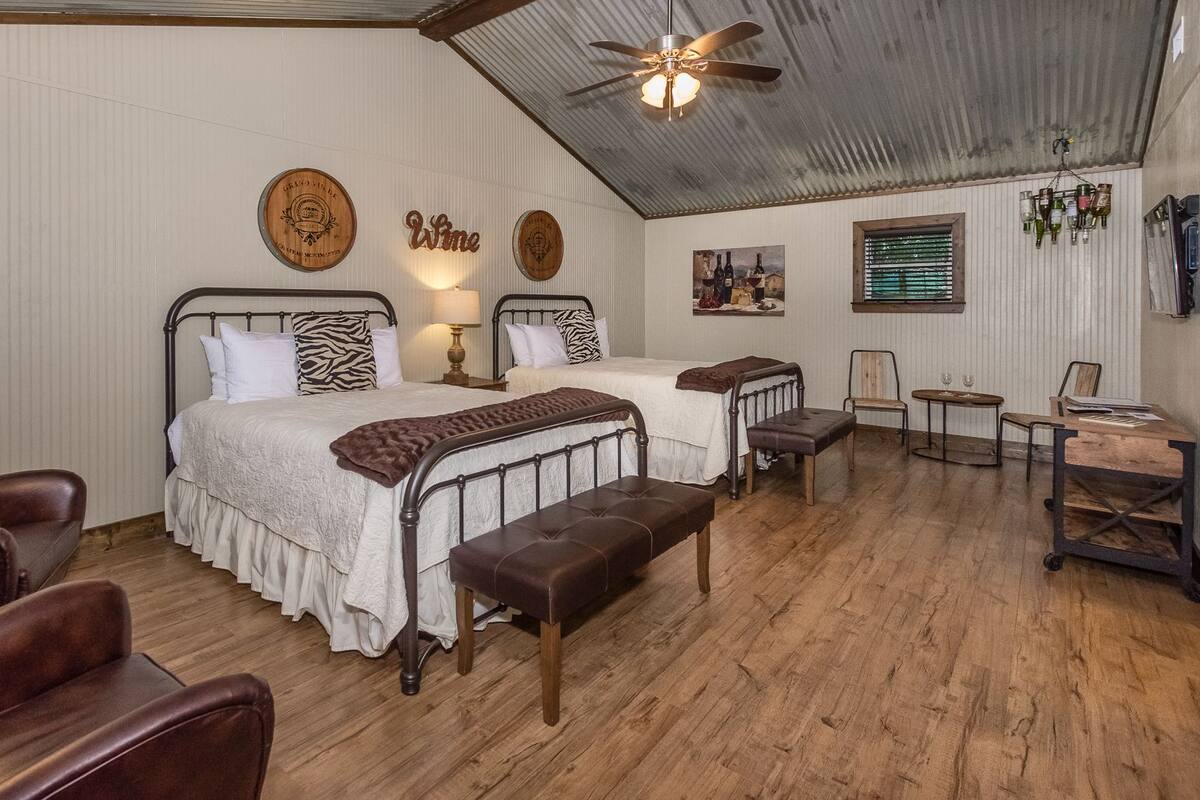 Una habitación con dos camas, un banco de madera, un escritorio y un ventilador de techo.