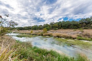 A river flowing through a natural landscape with trees and vegetation. - Vineyard Trail Cottages - Adults Only (Fredericksburg)