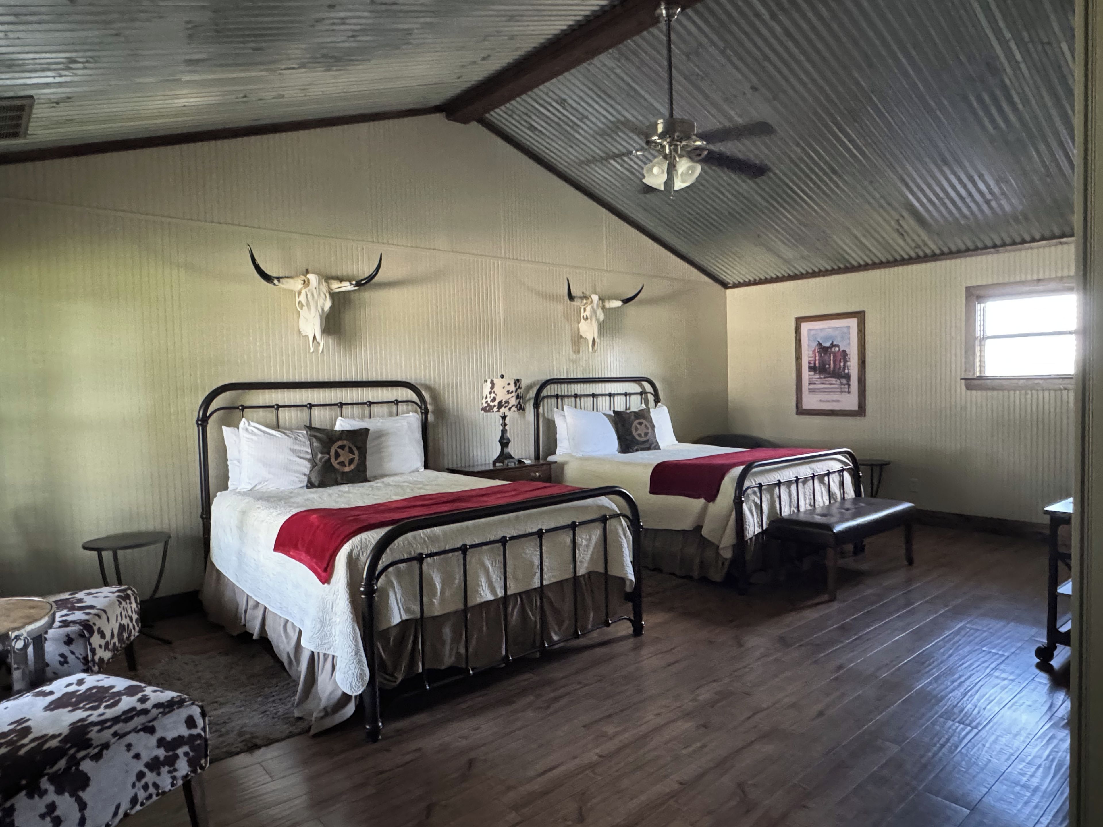A room with two beds, a ceiling fan, a framed picture on the wall, and a window.
