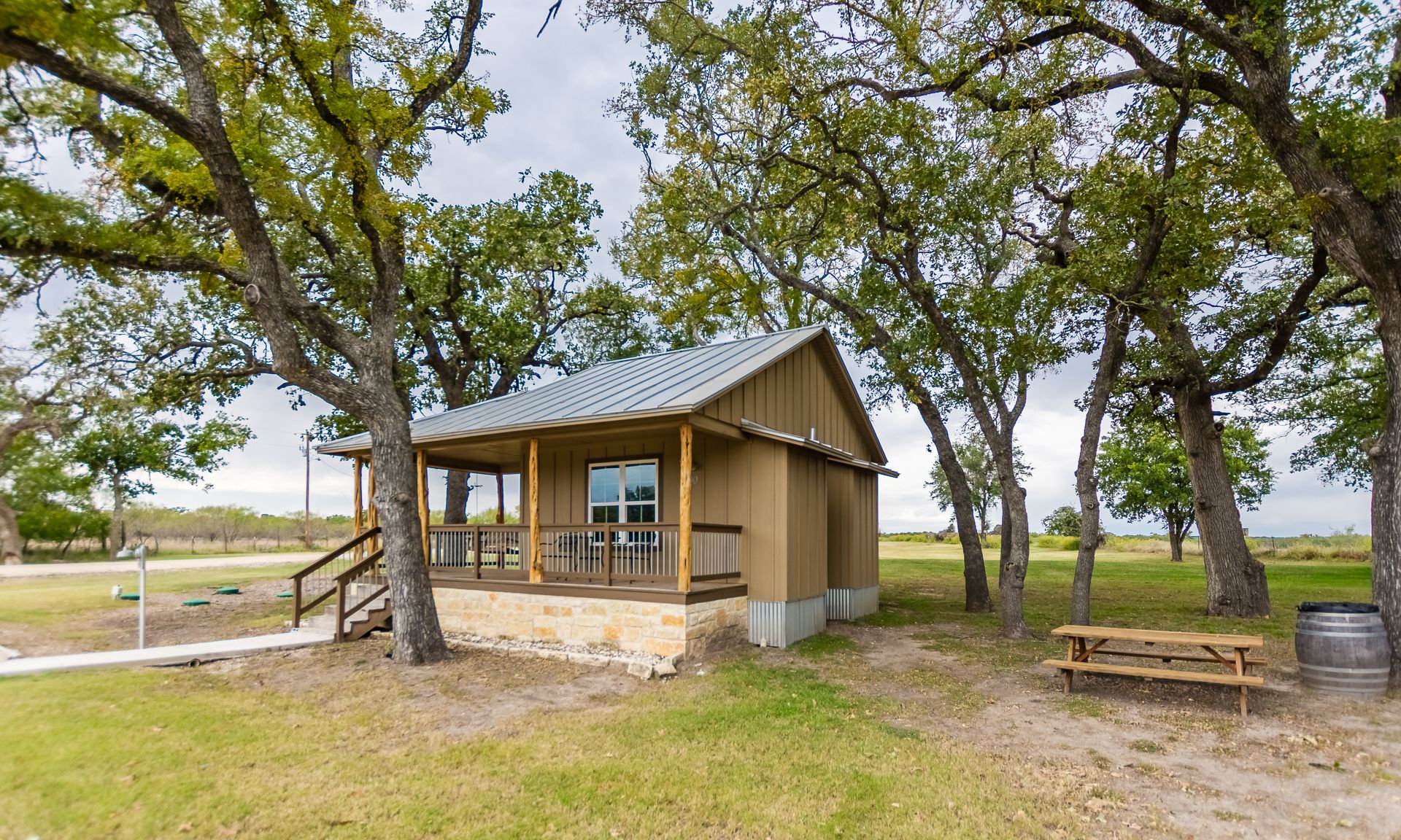 A small wooden cabin with a porch, surrounded by trees in a grassy area.