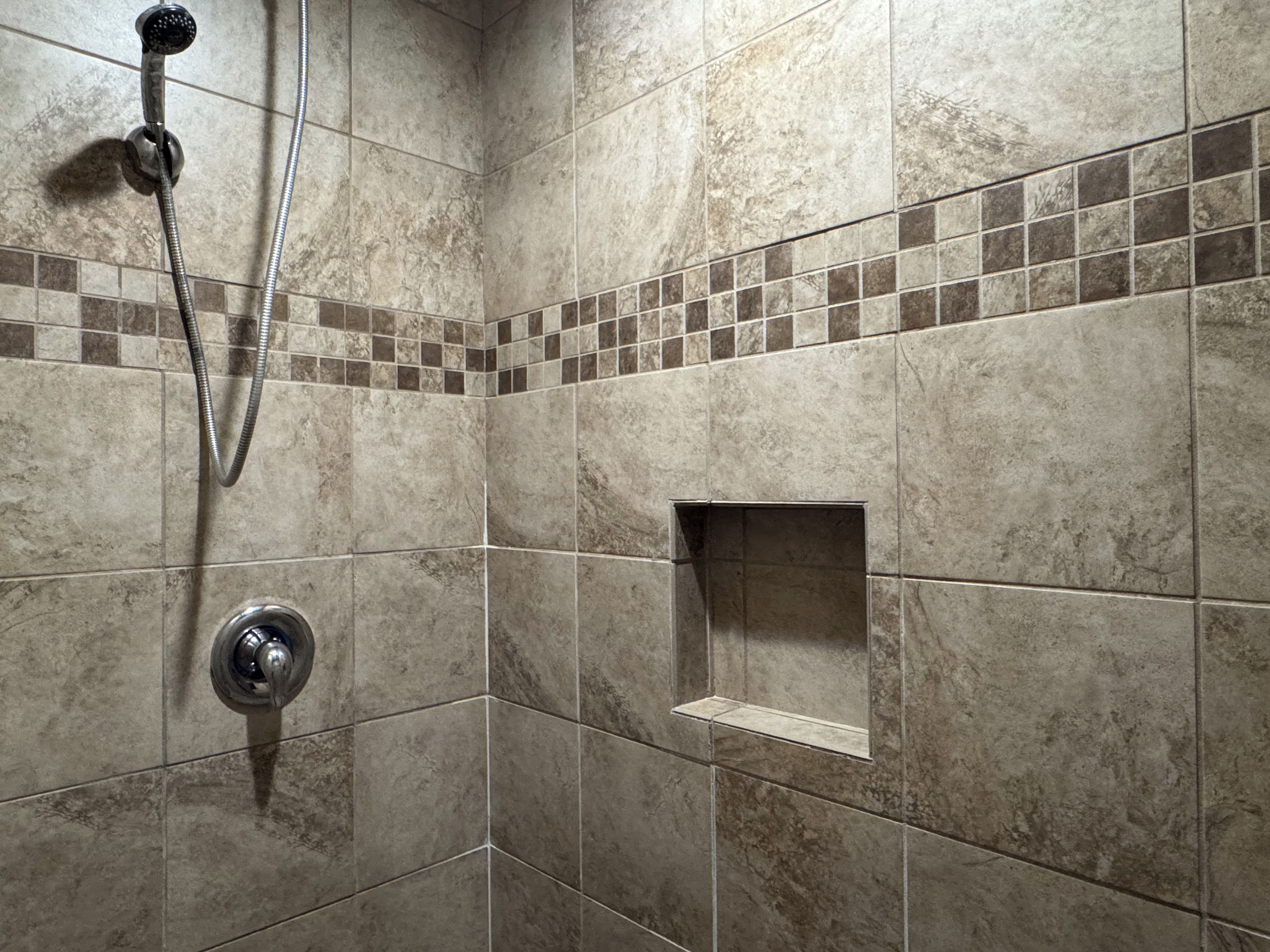 A shower area with a handheld showerhead and a wall-mounted faucet.