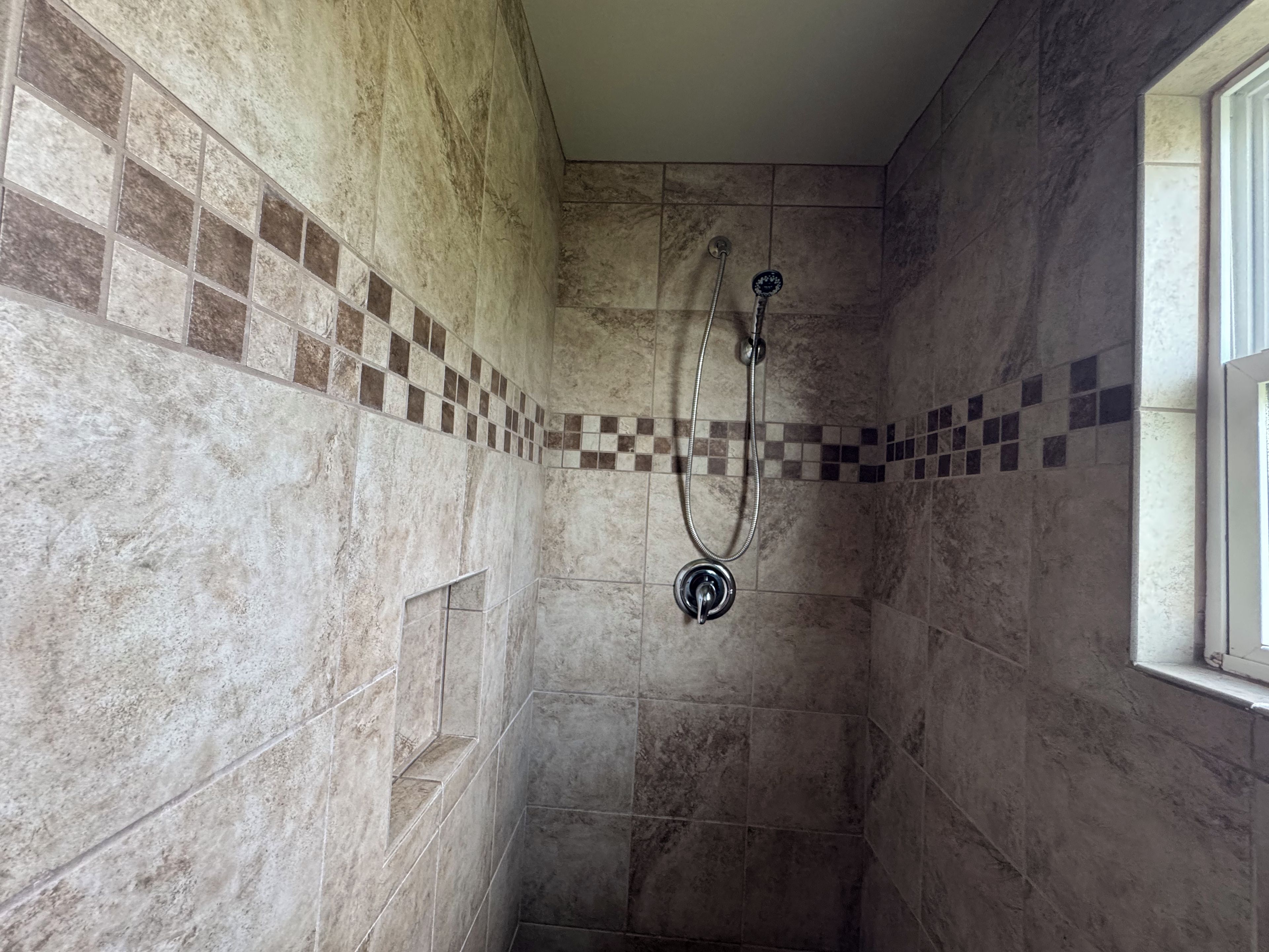 Ducha con pared de azulejos, un cabezal y una ventana.
