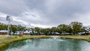 Una fuente rústica con un molino y una fuente, rodeada de cabañas de madera y árboles.
