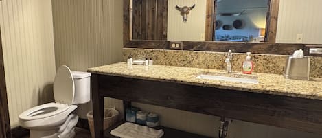 Ein Badezimmer mit einem Holzkosmetikschrank, Toilette, Spiegel mit Kuhschädel-Dekoration und Waschbecken mit Toilettenartikeln.