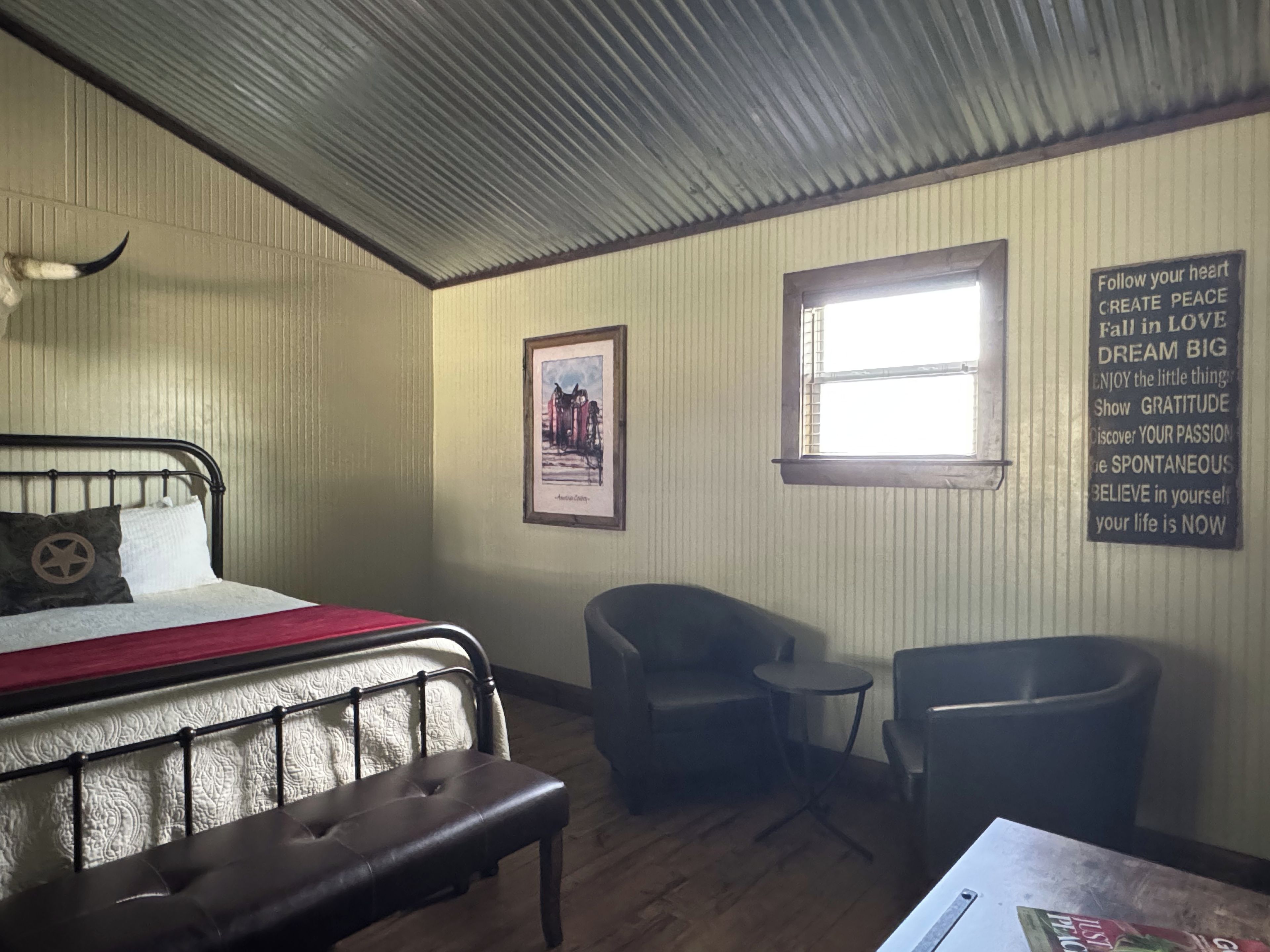 Ein Zimmer mit einem Bett, zwei Stühlen, einem kleinen Tisch, einem gerahmten Bild und motivierenden Wandbildern.