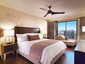 A hotel room with a large bed, a ceiling fan, a view of the city, and a cityscape through the window.