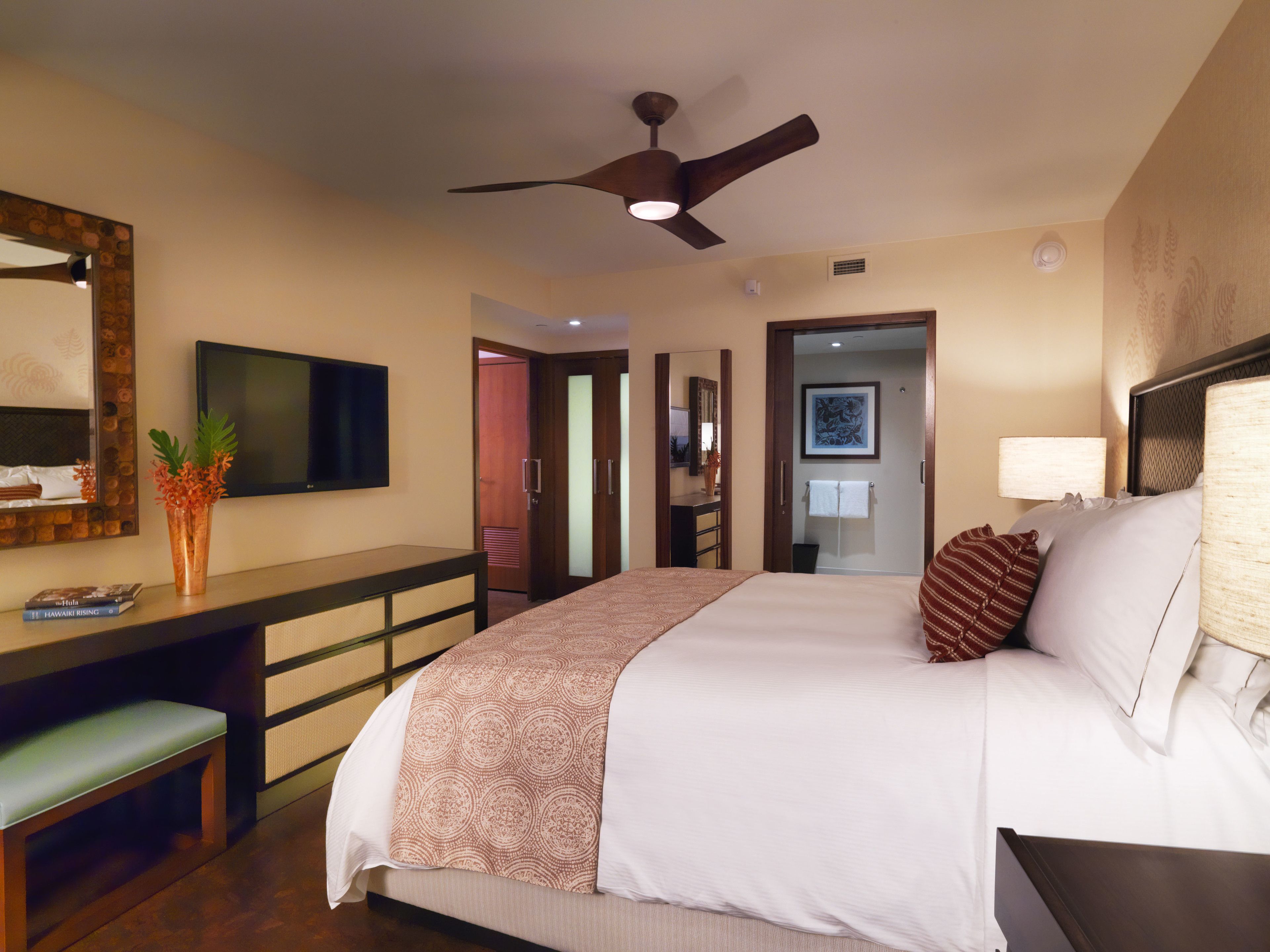 A hotel room with a bed, a desk, a TV, a ceiling fan, and a bathroom door.
