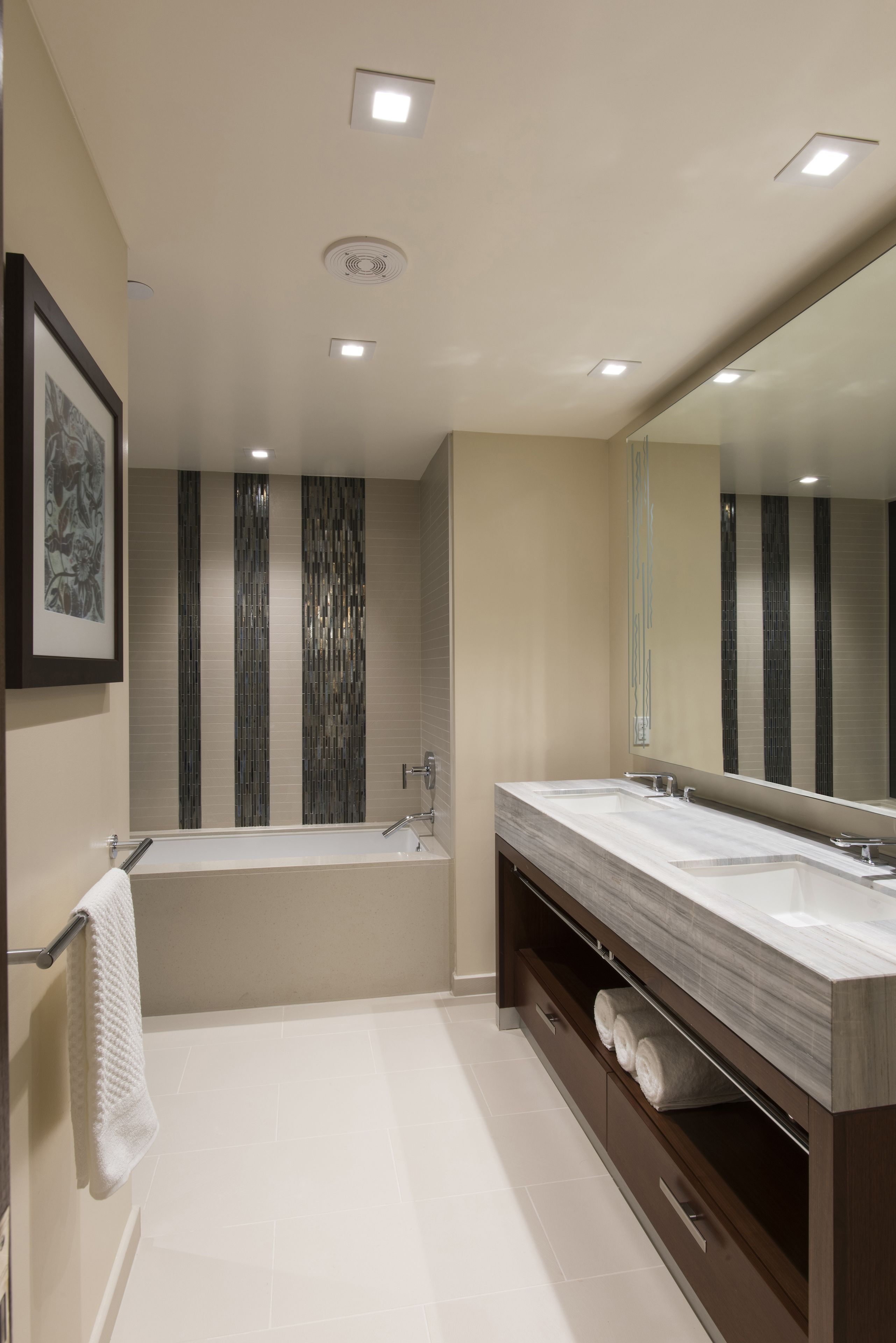 A modern bathroom with a large mirror, dual sinks, and a bathtub.
