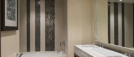 A modern bathroom with a large mirror, dual sinks, and a bathtub.