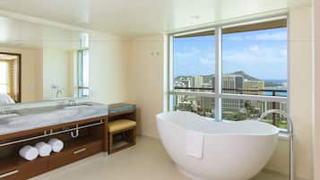 A modern bathroom with a large bathtub, a marble vanity, and a large window offering a city view.