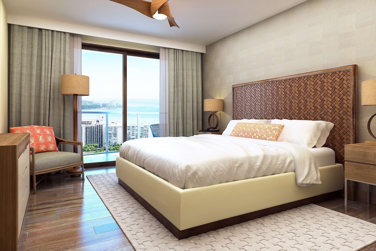 Ein modernes Hotelzimmer mit einem großen Bett, einem Schreibtisch, einem Sessel und Blick auf Stadt und Meer.