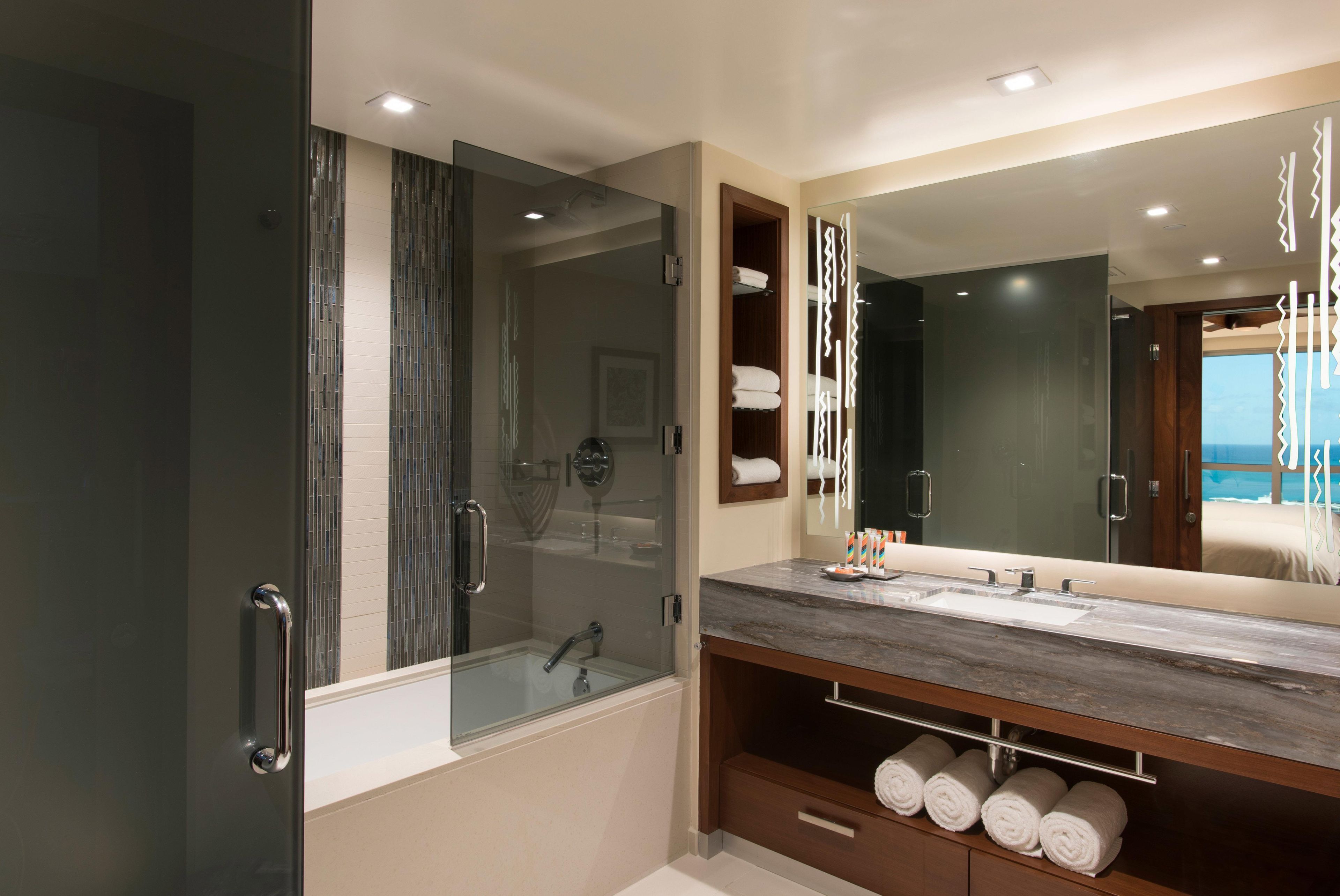 A modern bathroom with a glass-enclosed shower, a large mirror, and a marble countertop.
