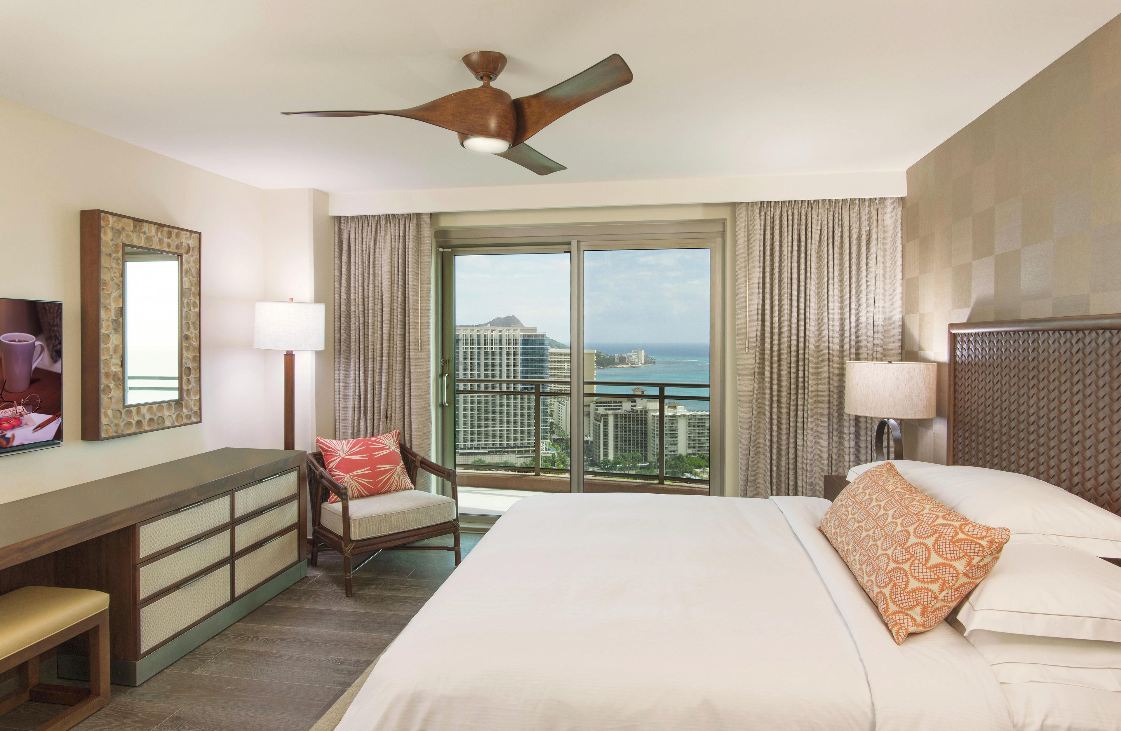 A hotel room with a bed, a desk, a chair, a ceiling fan, and a large window with a city view.