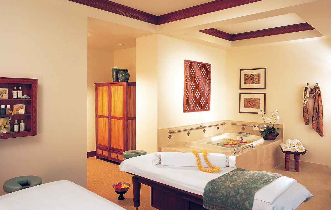 A spa room with a massage table, a bathtub, and a wooden cabinet.
