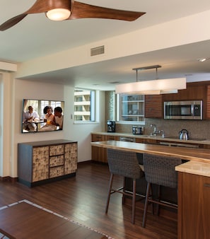 A modern kitchen with wooden cabinets, a stainless steel microwave, and a large island with bar stools. - Hilton Grand Vac Club The Grand Islander Waikiki Honolulu (Honolulu)