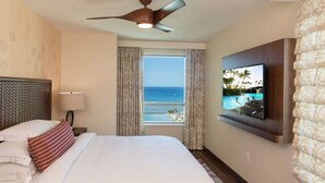 A hotel room with a bed, a TV mounted on the wall, a ceiling fan, and a window with a view of the ocean. - Hilton Grand Vac Club The Grand Islander Waikiki Honolulu (Honolulu)