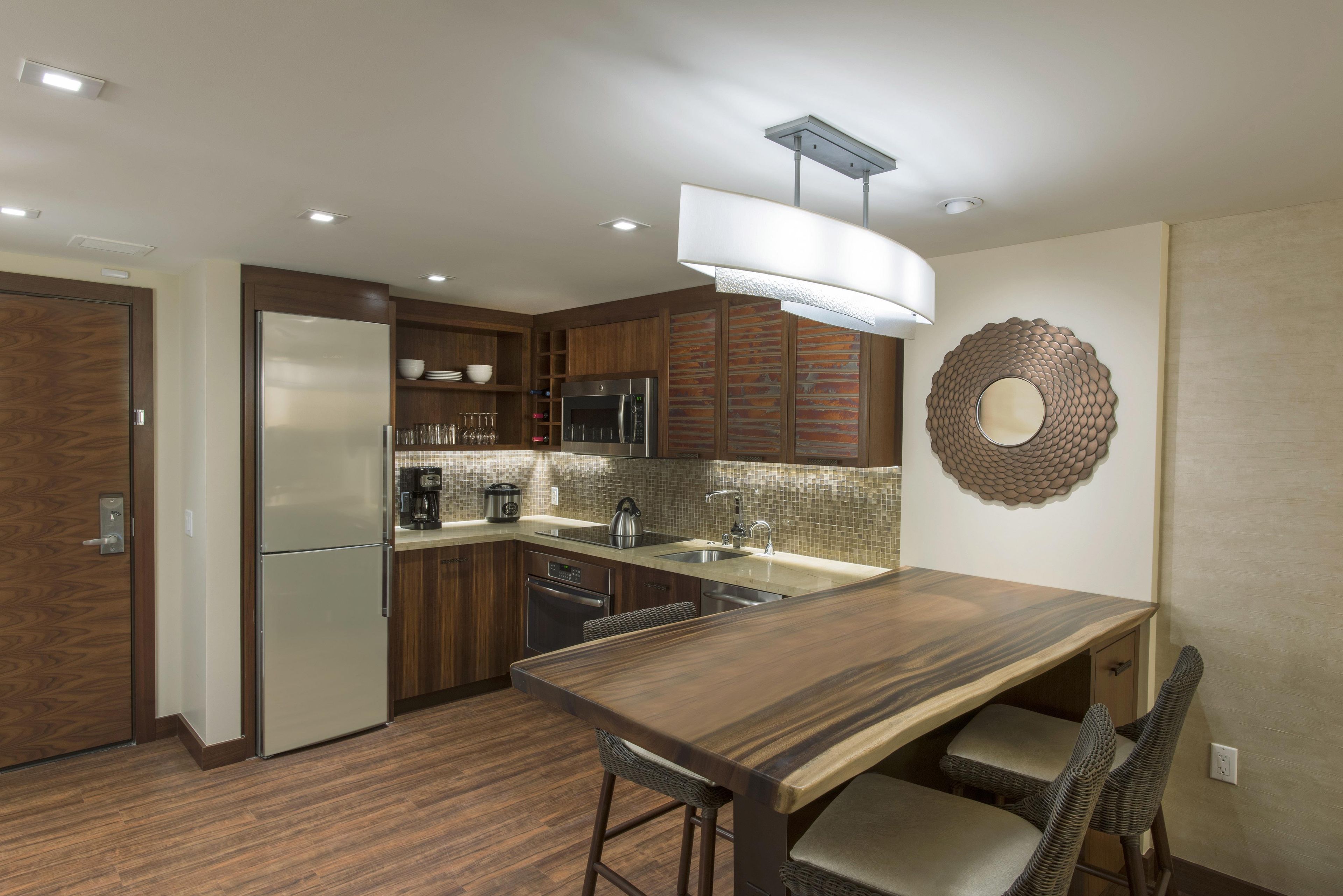 A modern kitchen with a built-in refrigerator, microwave, and stove. There is a dining table with bar stools and a decorative wall piece.