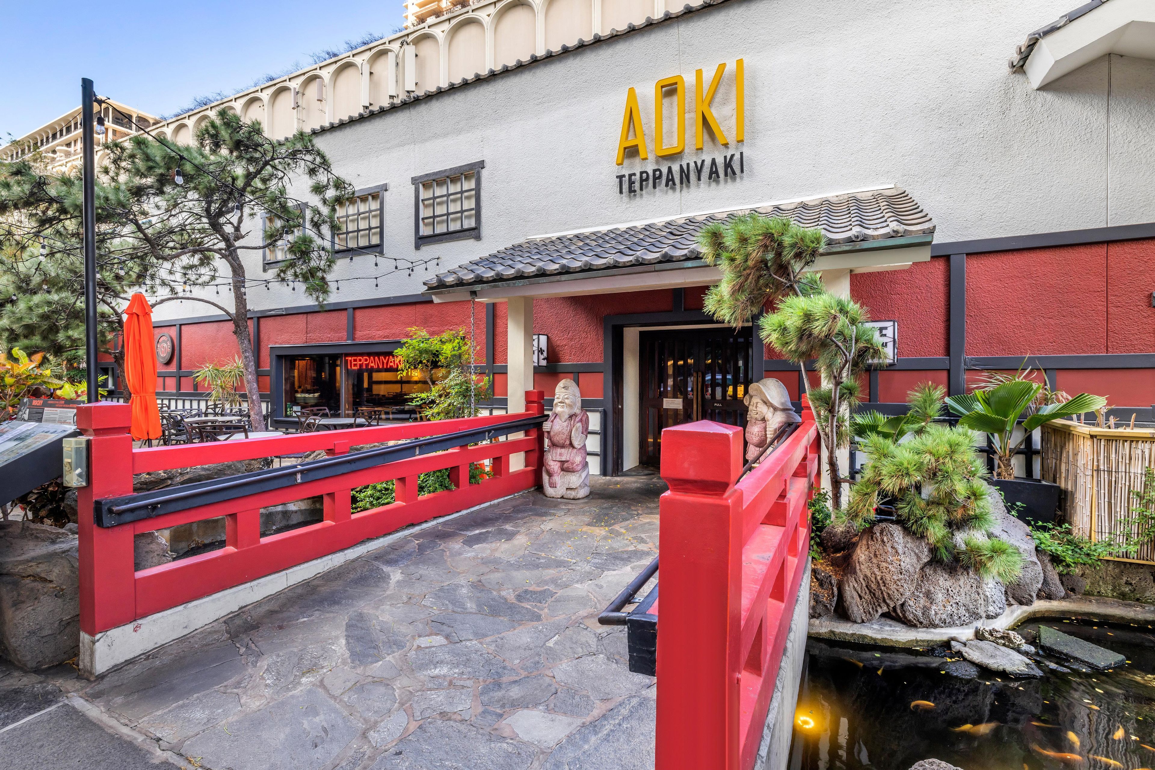 A restaurant named 'ADKI' with a red exterior, stone flooring, and a small pond with fish.