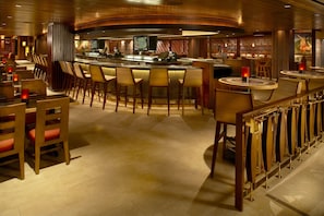 A bar area with wooden bar stools, a counter, and a television screen. - Hilton Grand Vac Club The Grand Islander Waikiki Honolulu (Honolulu)