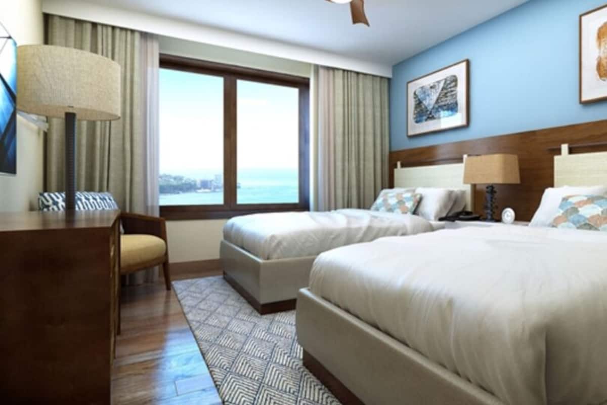 Ein Hotelzimmer mit zwei Betten, einem Schreibtisch, einem Stuhl, einer Lampe und einem Fenster mit Aussicht.