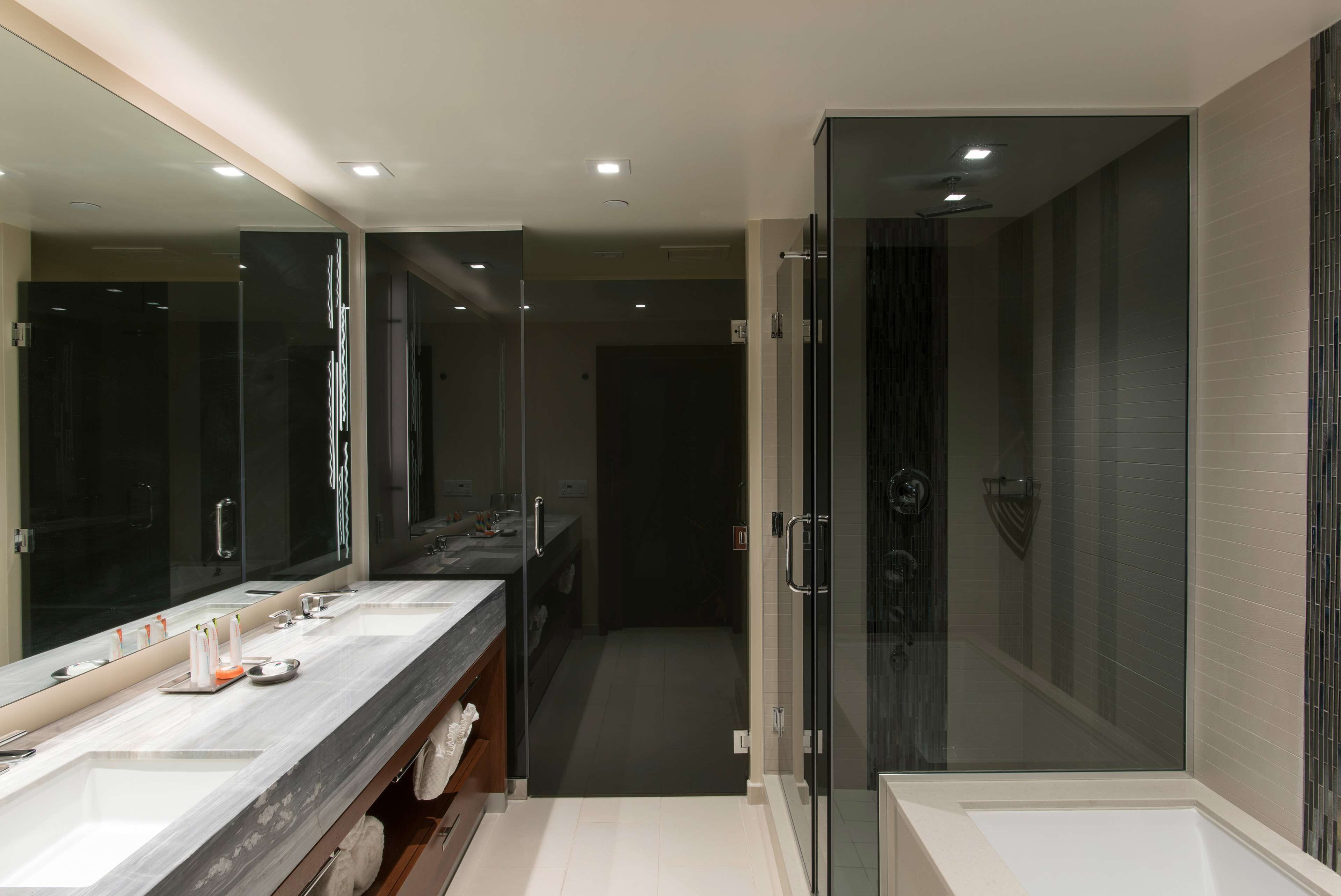 Une salle de bain moderne dotée d’un grand miroir, de deux vasques, d’une douche et d’une douche à l’italienne avec des parois en verre.