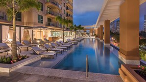 A poolside area with lounge chairs and palm trees, surrounded by a modern building with balconies. - Hilton Grand Vac Club The Grand Islander Waikiki Honolulu (Honolulu)