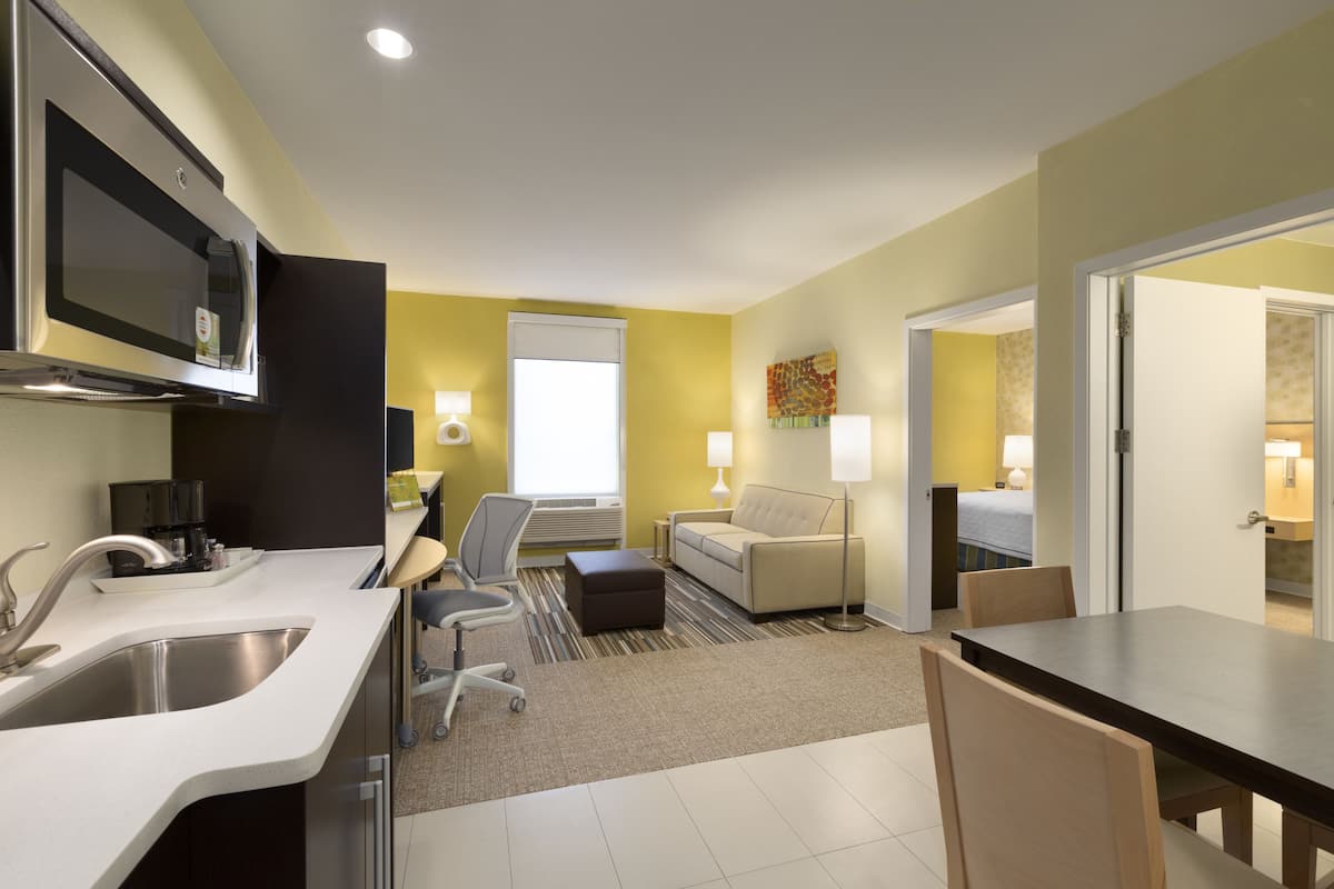 A modern kitchen with a microwave, sink, and dining area. There is a sofa and a small table in the living area.