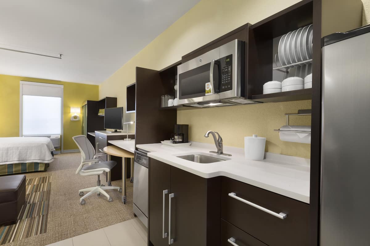 A modern hotel kitchen with a microwave, sink, and stainless steel appliances.