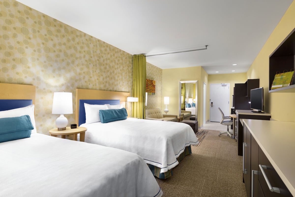 A hotel room with two beds, a desk, a chair, a television, and a door leading to another room.