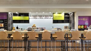 A modern coffee shop with multiple seating areas, a counter with a menu, and branded signage. - Home2 Suites by Hilton Houston Pasadena (Pasadena)