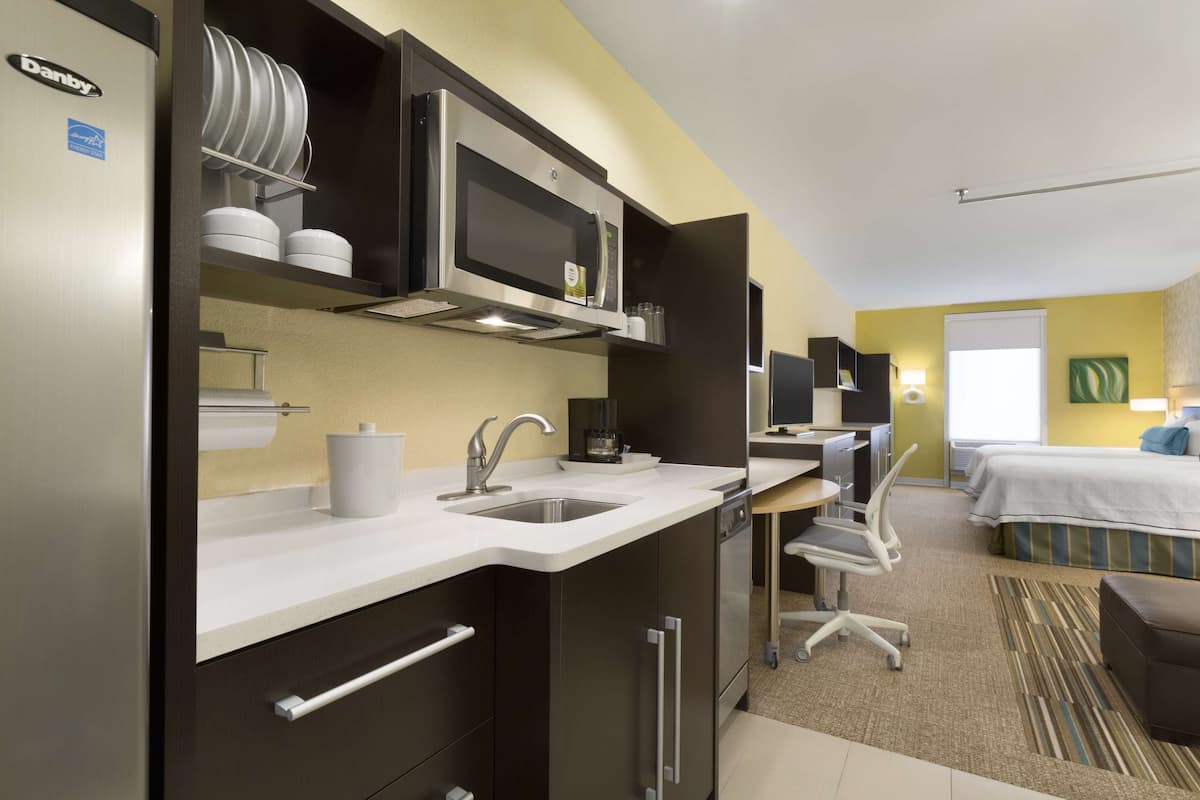 A compact hotel room with a kitchenette, a bed, a desk, and a bathroom.