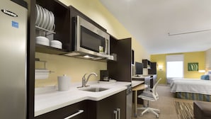 A compact hotel room with a kitchenette, a bed, a desk, and a bathroom. - Home2 Suites by Hilton Houston Pasadena (Pasadena)