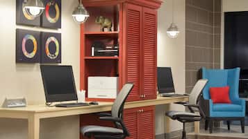 A modern office space with a wooden desk, two computer monitors, office chairs, a red filing cabinet, and a blue armchair.