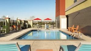 A swimming pool with lounge chairs and umbrellas, surrounded by a fence and a building. - Home2 Suites by Hilton Houston Pasadena (Pasadena)