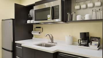 A compact kitchen with a stainless steel refrigerator, a microwave, a coffee maker, and a sink.