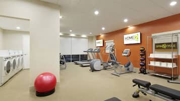 Een sportschool met trainingsapparatuur, een loopband, een crosstrainer, een hometrainer en een rode fitnessbal.