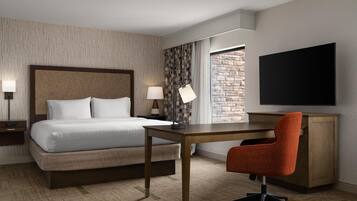 Hotelkamer met een bed, bureau, stoel, televisie en uitzicht op een stenen muur.