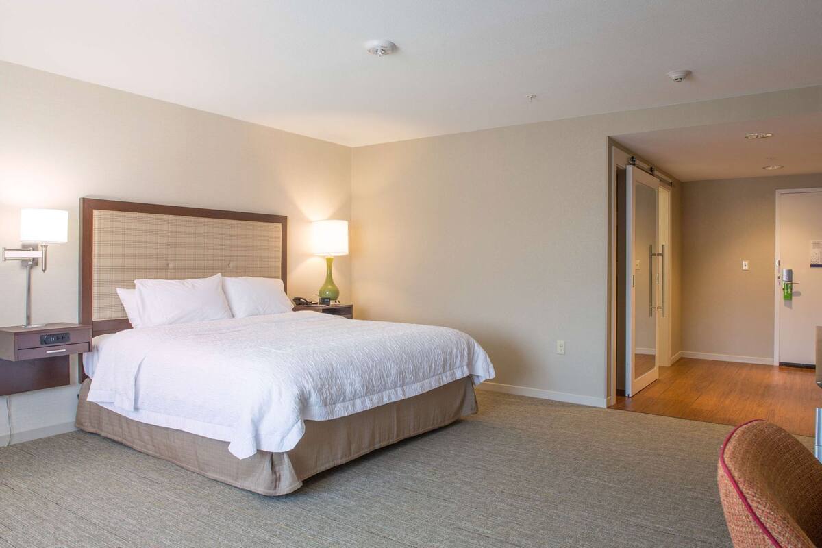 A hotel room with a large bed, bedside lamps, a nightstand, and a chair.